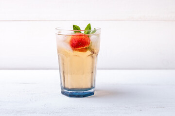 a glass of iced tea with strawberries and mint on a white wooden background. soft drinks in the heat