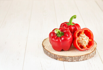 Red ripe peppers lie on a wooden round stand on a white table