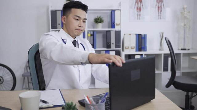 japanese man physician at desk is closing laptop lid with a sigh of relief after completing work and gazing into the distance considering in his personal office