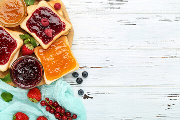 Toasts with jam and fresh berries on white wooden table