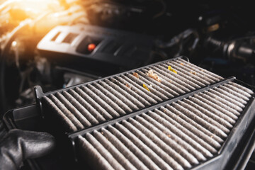 Car air filter is dirty in a hand with the engine blurred backdrop