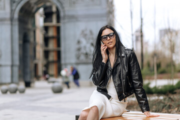 Young beautiful brunette in sunglasses and fashionable outfit talking on the phone in the street