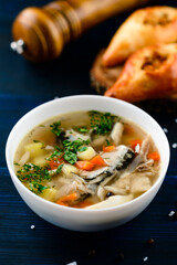 Hot tasty healthy soup with fish and vegetables served on a round plate on wooden table