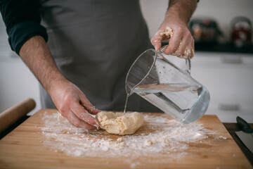 A male chef prepares noodle dough at home in the kitchen. Close up of hands with flour and dough