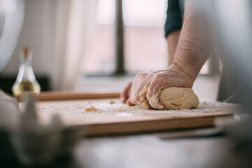 A male chef prepares noodle dough at home in the kitchen. Close up of hands with flour and dough