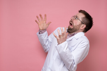 Frightened, amazed doctor in a white coat looks in fear and throws hands up. Copy space. Pink background.