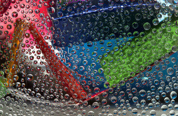 Translucent water droplets fall down against the pink-blue-gray background with multicolored geometric figures. Abstract fantasy. 3D render. 