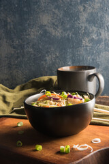 Egg roll bowl topped with shallots. Cup of tea. Chop sticks, green napkin  on wooden cutting board.