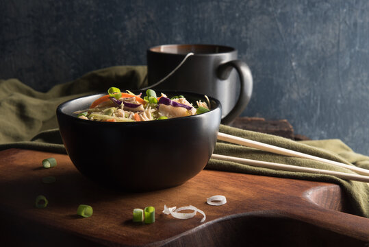 Close Up View Of Egg Roll Bowl Topped With Shallots. Salad. Cup Of Tea. Chop Sticks, Green Napkin  On Wooden Cutting Board. 