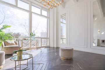 very light and bright interior of luxurious cozy living room with chic soft beige furniture with gold metallic elements, huge window to the floor and wooden parquet