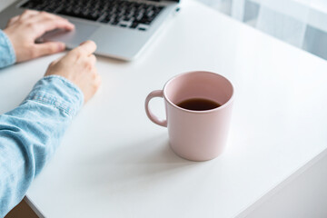 there is a pink mug on the table, next to a girl is typing on a laptop keyboard