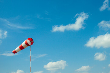 Windsock flag with red and white stripes on blue sky background. Wind speed meter