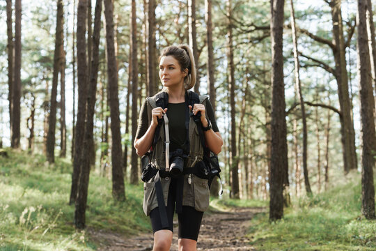 Hiker walking with a backpack and modern mirrorless camera in green forest