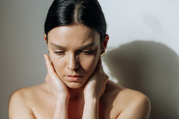 A beautiful brunette girl with clean healthy skin looks down with her arms around her neck. Portrait, horizontal photo