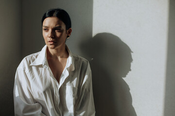 Beautiful young brunette stands in a white shirt under the rays of the sun