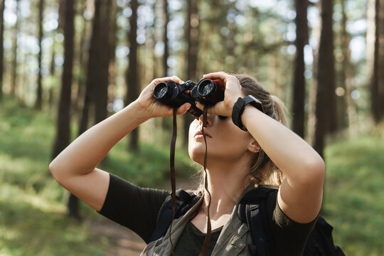 Female hiker is using binoculars for bird watching in green forest