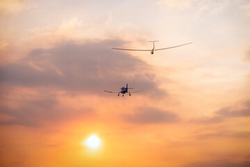 Fototapeta na wymiar a glider sailplane towed by a small private airplane toward the evening setting sun with orange clouds