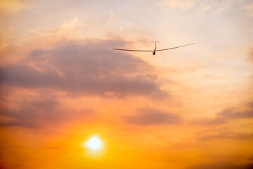 a glider sailplane soaring toward the evening setting sun with orange clouds