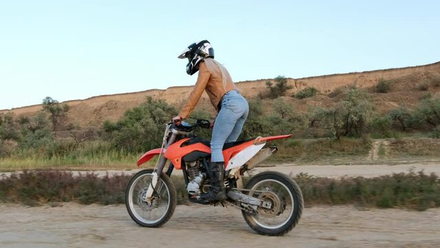 The girl is an amateur motocross, rides on a sports motorcycle on the beach against the background of the hills.