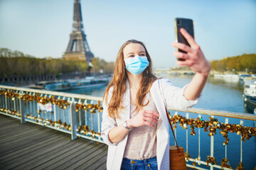 Young girl standing near the Eiffel tower in Paris and wearing protective face mask during coronavirus outbreak