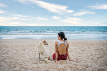 Young asian woman sitting with a dog on the beach in tropical sea on vacation