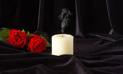 An extinguished candle and a red rose on a black background. The concept of mourning, condolences,...