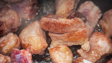 Fried pieces of meat close-up, pork from fatty meat at home. Food cooked in a pan. Very bold. Delicious frying of meat products. Cooking in a rustic style, top view. pieces of meat are fried in oil