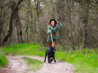 Young lady in country style fashionable clothes walking with hunting dog along the spring forest path