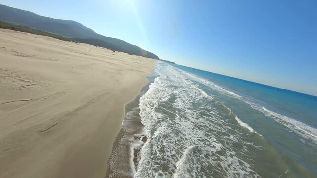 Dynamic Aerial Footage Shot on FPV Drone Flying Above empty Wide Long Sand Beach and Ocean Surf. Sea Waves on Patara Beach in Likya, Turkey.