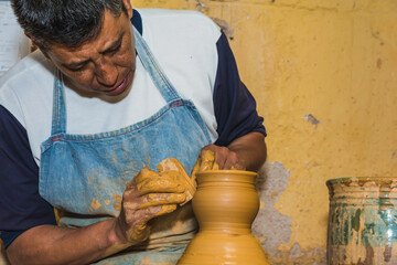 Mexican potter craftsman, working the clay with his hands in his workshop to create sculptures,...