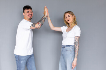 Image of friendly young people man and woman in basic clothing laughing and giving high five...