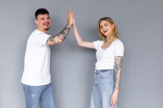Image of friendly young people man and woman in basic clothing laughing and giving high five isolated over gray background
