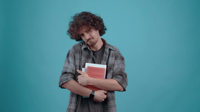 The charismatic chalky young man holds a few books in his hand and emphasizes the need to read by positioning his index finger on his head. Isolated on a turquoise background. Concept of life. People