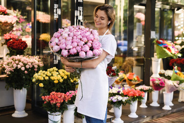 Woman florist with a heap of pink peony flowers in her little flower shop