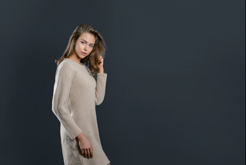 Fototapeta premium a young attractive girl in a beige warm jacket on a black background is copying the space. long knitted jumper on a beautiful girl