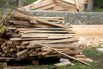 A pile of sloppily folded dry new wood-burning planks lying on the street in a vegetable garden at a cottage or a private house on the ground against the background of building materials outside.