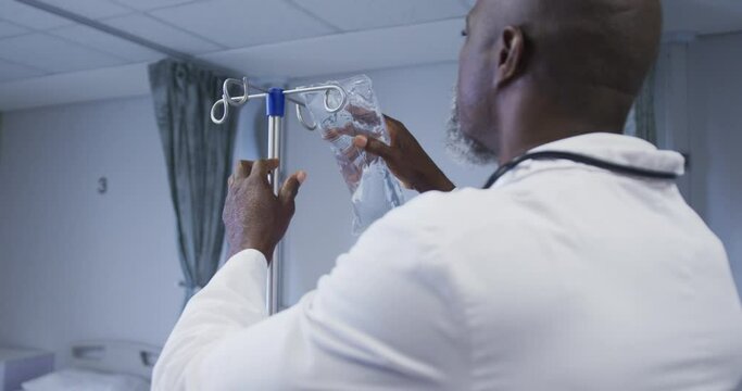 African american male doctor preparing drip bag for patient in hospital room
