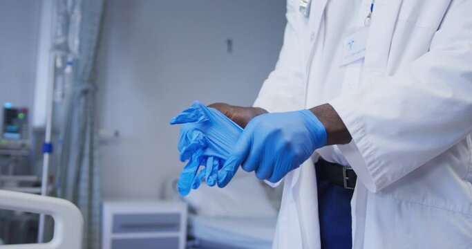 Midsection of african american male doctor wearing latex gloves in hospital patient room