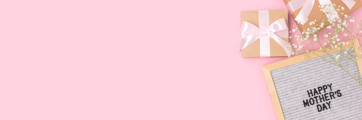 Happy Mothers day. Banner with letter board, white gypsophila flower, gifts tied with ribbons on a pink background.