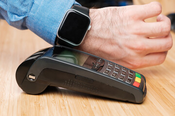 Customer paying through smartwatch using NFC technology. Contactless payment terminal machine.