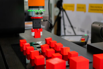 Pick and place robotic clamp arm manipulator moving red toy blocks at modern robot exhibition,...