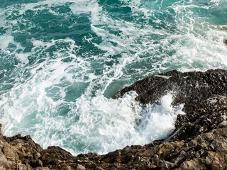 Top-down view of waves crashing on the rocky shore.