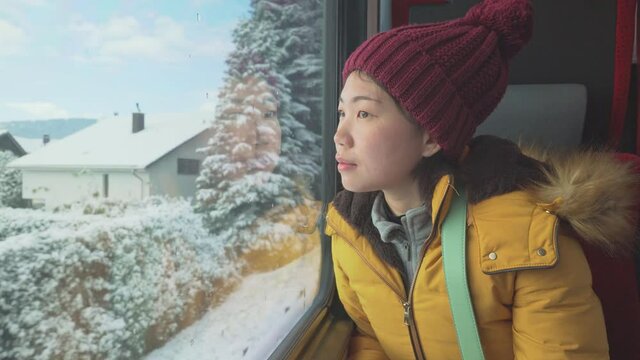 train travel getaway - young happy and beautiful Asian Japanese woman enjoying snow landscape through railcar window during Winter holiday trip
