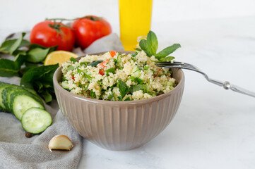 Traditional oriental salad Tabouleh with couscous or bulgur on a white marble background.