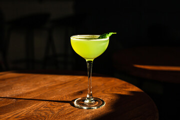 A sweet and sour refreshing basil gin sour cocktail in a coupe glass in direct hard sunlight with...