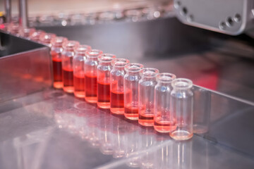 Pharmaceutical automatic production line machine conveyor with glass bottles with red liquid at pharmacy processing factory - close up. Pharma, medicine, vaccination, automated technology concept