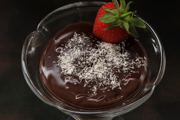 Chocolate pudding in a glass bowl, coconut and strawberries on it. Local name Supangle