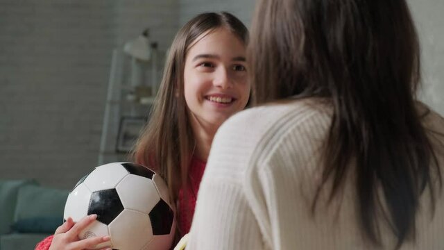 Close up of a happy girl that is talking with her mother while they eat a banana, girl holds a ball in her hand.