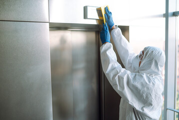 Cleaning and disinfection of the elevator to prevent COVID-19. Worker wearing protective suit...