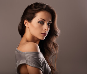 Beautiful mysterious woman makeup face and healthy volume brown hair with wisdom emotional look on brown color background. Closeup